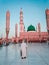 An old Muslim man walks towards masjid Al Nabawi minaret and green dome in Madinah, Saudi Arabia