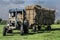 Old neglected blue tractor pulling a triler of hay in a field at harvest time