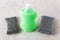 Old and new silver foam sponges near green dishwashing liquid on a kithen table. Metallized fiber foam sponge for dishes and