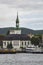 An Old Norwegian Church with an ornate copper weathered tower sits at the waterfront, in an older part of the city of Bergen.