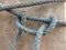 Old nylon ship ropes tied to knot bound around cement electrical post on ground flooring closeup.