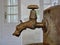 Old ornamental metallic spring water tap with water drop at faucet mouth and white door in the background