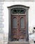 Old ornate brown double house door with broken repaired panels and hand shaped knocker with stone frame and doorstep
