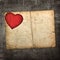 Old paperboard card with red paper heart on a dark fabric backgr