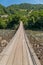 An old pendant wooden bridge across a stormy river in the background of mountains will help you to move from one shore