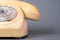 Old plastic landline telephone on a gray background. Retro yellow phone with handset, rotary dialer and holes with