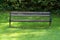 Old public park bench with wooden boards and baroque style wrought iron supports surrounded with fresh green grass and dense hedge