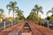 Old rail line transformed into a walking sidewalk between palm trees and some benches to s