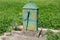 Old rarely used rusted outdoor metal water pump with large rotating handle mounted on concrete stand