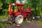 An old red agricultural tractor stands in the forest during repairs and maintenance with the wheel removed and the dismantled