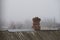 Old red brick chimney on a roof covered with corrugated asbestos-cement sheet, autumn foggy rural landscape