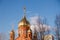 Old red brick Christian church with golden and gilded domes against a blue sky and tree branches. Concept faith in god, orthodoxy