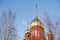 Old red brick Christian church with golden and gilded domes against a blue sky and tree branches. Concept faith in god, orthodoxy