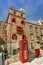 An old red cardphone booth in the historic city Valletta with an old appartment building in the background