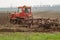 An old red crawler tractor plows a field. Green grass in the foreground