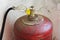 Old red gas cylinder with valve and gas supply hose standing on the floor near the wall