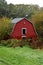 Old red hipped roofed barn surrounded by trees and bushes