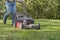 Old red push lawn mower cutting grass in blue jeans sunny shady spring day