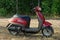 Old red scooter stands in the grass in the park