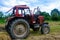 Old red tractor in the field during the haymaking season, pressing hay on bales, forage harvesting