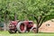 An old red tractor under old apple trees in garden waiting to get back to work