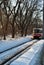 Old red tram in snowy park, railroad along trees line, winter sunny day
