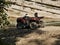 An old red two-seater Quad bike without a driver near a small mountain river on a background of rocks and green trees.