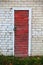 Old red wooden plank door with a lock in white brick wall