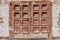 An old retro shabby wooden painted brown double door with a lock and a fragment of an old plastered wall with bare bricks