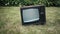 An old, retro TV is standing on grass. There is interference on the TV screen