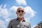 Old rich man with sun glasse and beard on street portrait, clouds in background