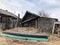 An old rickety wooden hut with boarded-up windows. There is dry grass and trees all around. The house is falling apart