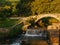 Old Roman stone bridge with waterfall over stream at sunset with soft golden light