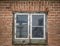 Old rotten double leaf window with mold and moss in brick wall.