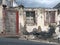 Old ruined house partly collapsed on a sloping street with a blocked up door crumbling walls and fading red painted windows