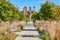 Old ruins at end of long walkway lined with benches and fall grasses