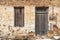 Old rural home facade. Weathered stonewall cottage exterior, wooden brown window and door. Greece