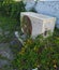 Old rusted outdoor split AC unit covered with tree brunches