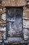 An old, rustic and deteriorated wooden door framed in a blue-gray tone on a stone wall in warm tones