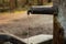 Old rustic drinking water fountain in the forest. Wooden construction, rusty metal pipe and faucet, streaming water. Close up shot