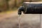Old rustic drinking water fountain in the forest. Wooden construction, rusty metal pipe and faucet, streaming water. Close up shot