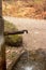 Old rustic drinking water fountain in the forest. Wooden construction, rusty metal pipe and faucet, streaming water. Close up shot