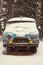 An old rusty ambulance van stands in a snow-covered clearing on a cloudy winter day.