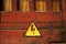 Old rusty black and yellow triangular hazard sign hanfing on brown painted wooden door