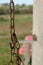 Old rusty chain and chain links, against a bokeh landscape, with a wooden pole and pink seat in the background, Block