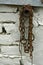 Old rusty chain hanging near a brick wall painted white.