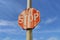 Old, rusty, faded Stop sign against blue sky with white wispy clouds