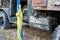 An old rusty flat truck with an open door is standing on the grass. A dirty Ukrainian flag hung in a knot hanging from a door