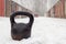 Old rusty heavy kettlebell for winter training on white snow covered road in garage community