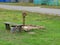 Old rusty iron well and wooden bench among green grass